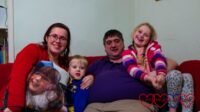 Me (holding the photo cushion with Jessica's photo), Thomas, Daddy and Sophie sitting on the sofa together