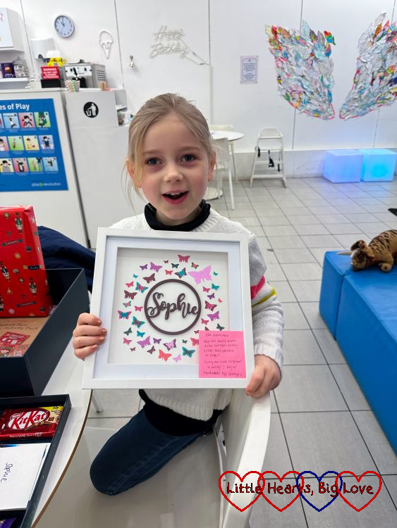 Sophie holding up a frame with her name surrounded by butterflies