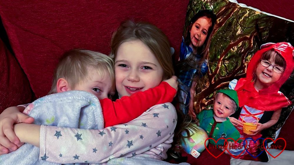 Thomas snuggled up to Sophie under a blanket on the sofa with a photo cushion of Thomas, Jessica and Sophie wearing fairytale costumes next to them