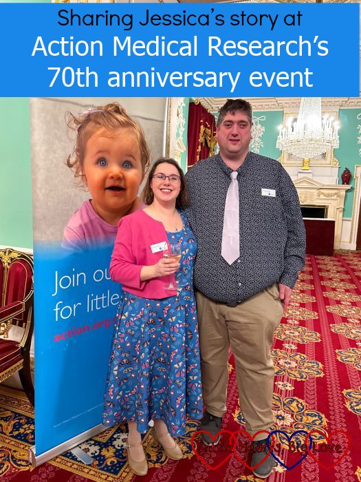 Me and my husband standing in front of a pull-up banner for Action Medical Research - "Sharing Jessica’s story at Action Medical Research’s 70th anniversary event"