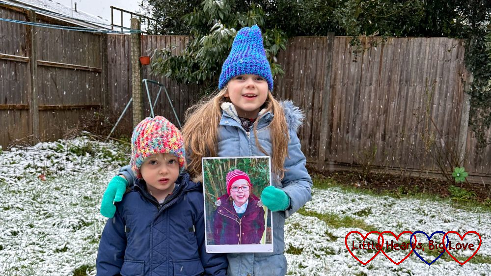 Sophie and Thomas standing in the snow in the garden with Sophie holding a photo of Jessica