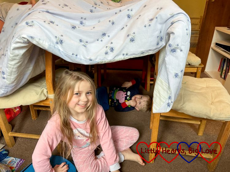 Sophie and Thomas inside a den made from chairs with a duvet over them