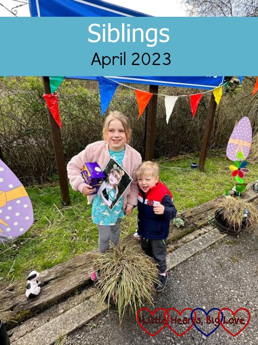 Sophie (holding an Easter egg and a photo of Jessica) and Thomas standing near cardboard cut out eggs - "Siblings - April 2023"
