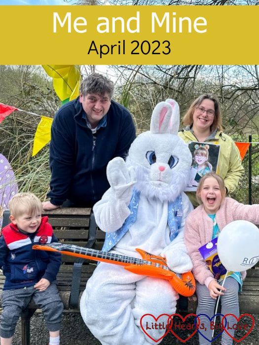 Thomas, my husband, me (holding a photo of Jessica) and Sophie sitting and standing around the Easter bunny who is sitting on a bench - "Me and Mine - April 2023"