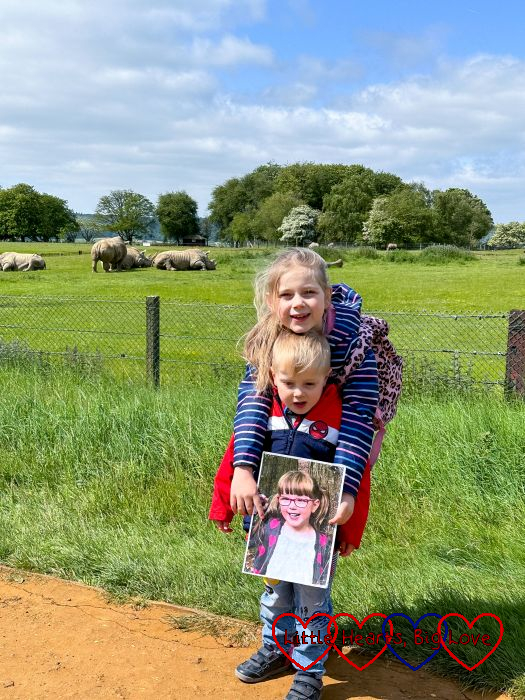 Sophie and Thomas holding a photo of Jessica in front of the rhino enclosure at Whipsnade Zoo