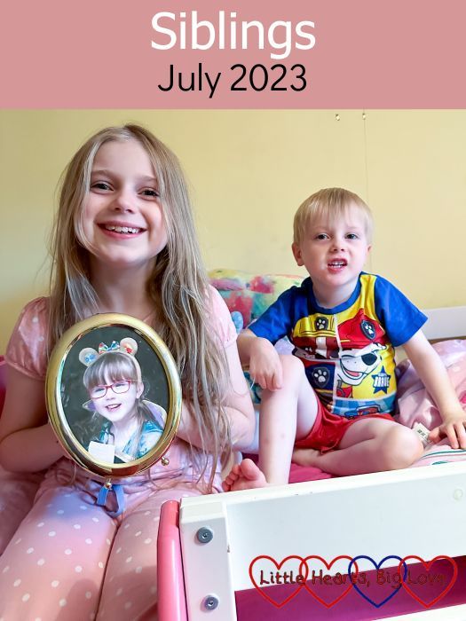 Sophie and Thomas sitting together on Sophie's bed with Sophie holding a picture of Jessica - "Siblings - July 2023"