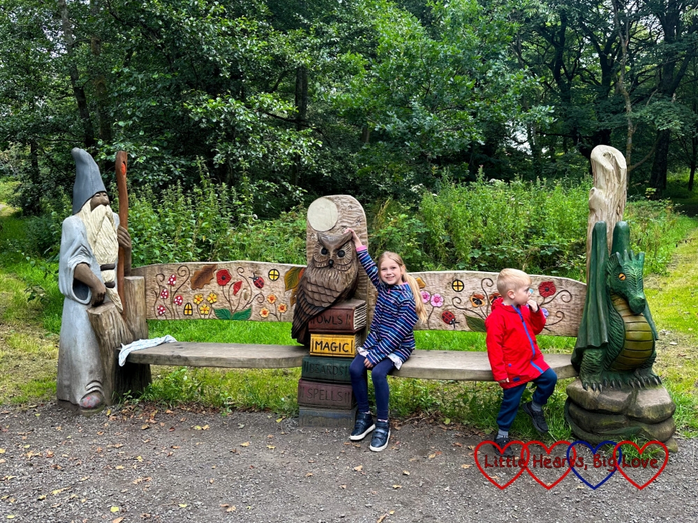 Sophie and Thomas sitting on a bench carved with a wizard at one end and a dragon at the other
