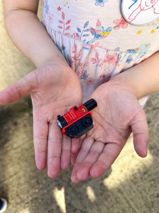 Sophie holding a geocache which is a small red model "James" from "Thomas the Tank Engine"