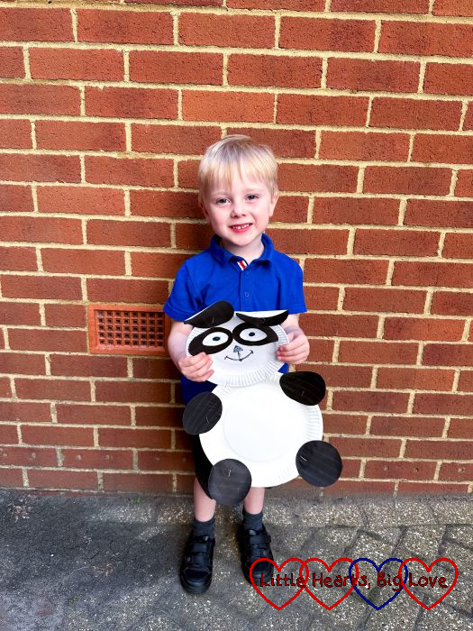 Thomas standing in front of a wall holding a panda made of paper plates.