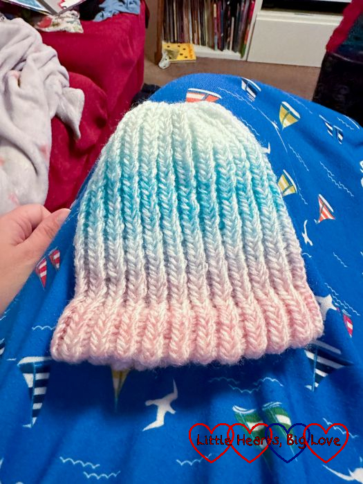 A white, pale yellow, pale blue and pale pink knitted baby hat