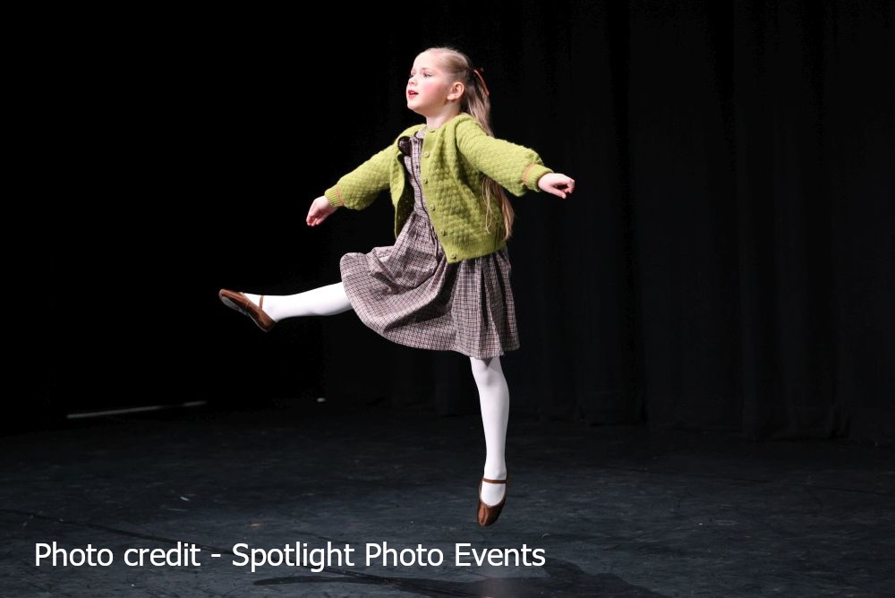 Sophie dancing her character solo, wearing a brown plaid dress, olive green cardigan, white ballet tights and brown ballet shoes.
