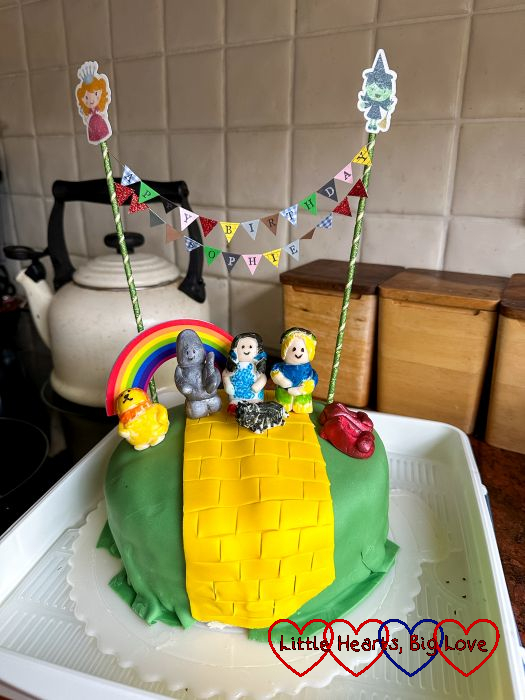 Sophie's Wizard of Oz themed birthday cake with bunting spelling out 'Happy Birthday Sophie', an icing yellow brick road and icing figures of Dorothy, the Scarecrow, Tin Man, Lion, Toto and the ruby slippers.