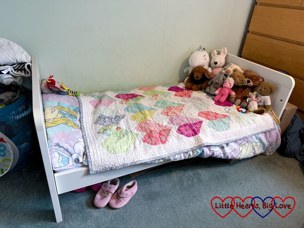 Jessica's bed with a heart-patterned quilt on top, a small collection of soft toys at the end of the bed and Jessica's favourite doll on her pillow. Her slippers are underneath the bed.