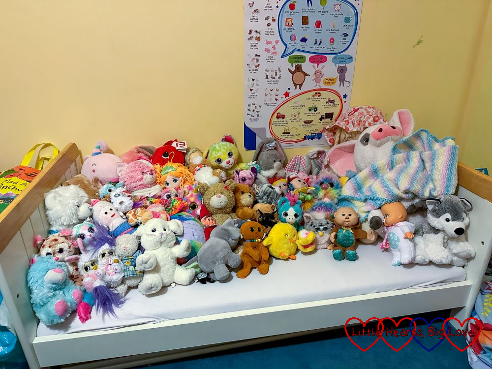 A collection of soft toys filling a toddler bed