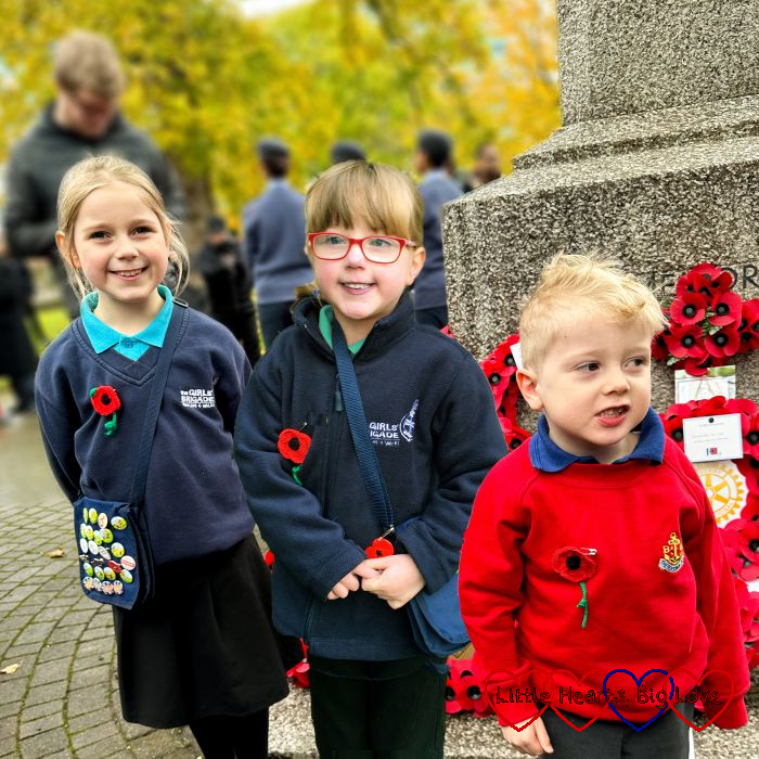Sophie, Jessica and Thomas in their Brigade uniforms standing in front of the poppy wreaths laid at the foot of the peace memorial