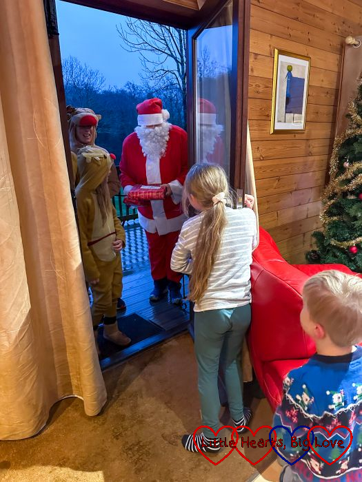 Sophie and Thomas opening the door of the lodge with Father Christmas and two people dressed in reindeer onesies standing at the door