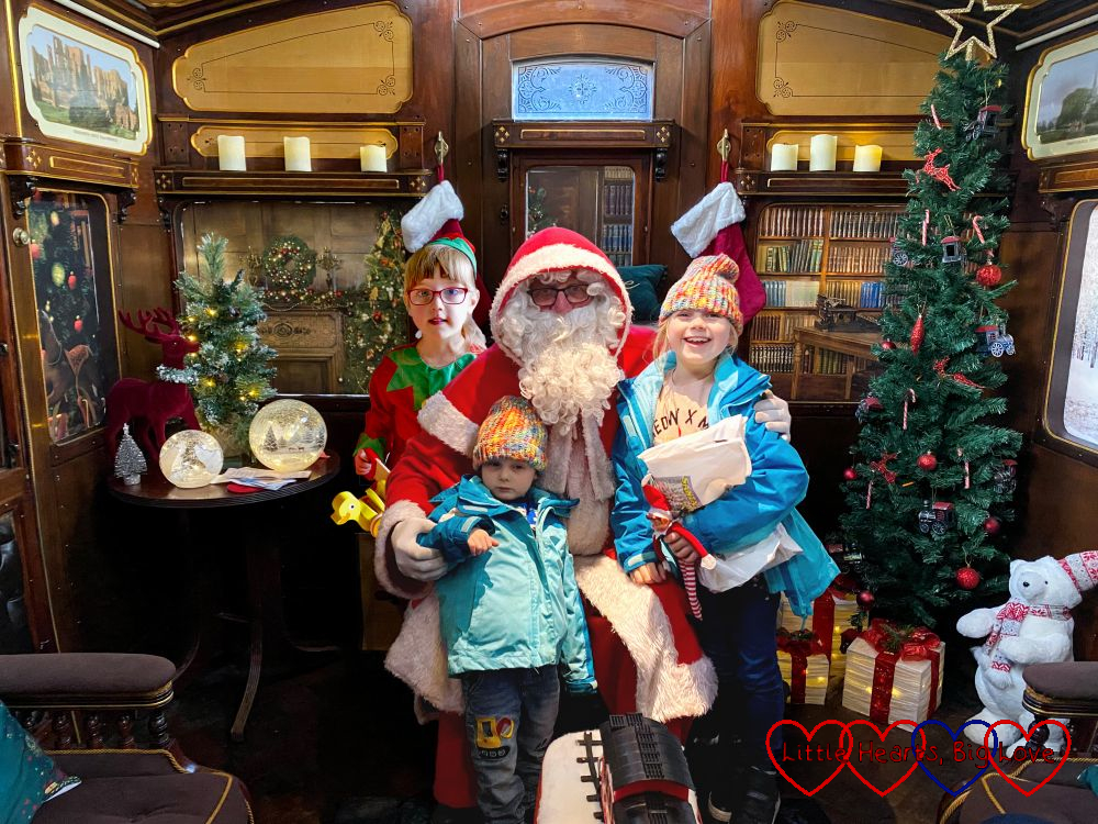 Sophie and Thomas with Father Christmas. Jessica is standing behind Father Christmas dressed as an elf.
