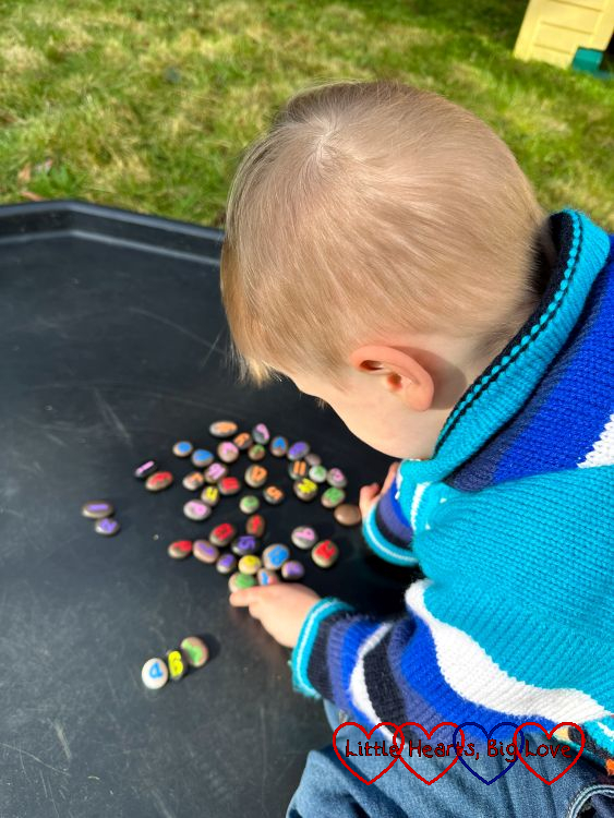 Thomas playing with his number and letter pebbles in the tuff tray in the garden