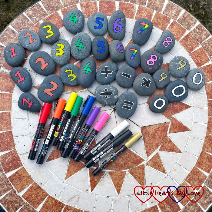 Pebbles painted with coloured numbers on a table with a selection of paint pens