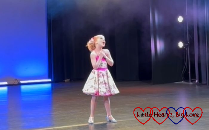Sophie wearing a flowery dress singing in her song and dance solo