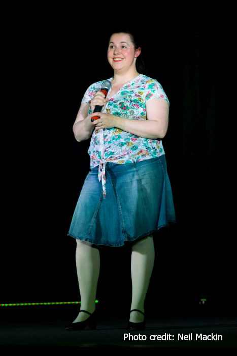 Me on stage wearing a flowery blouse and denim skirt and holding a microphone