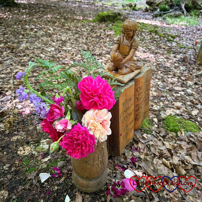 A wooden vase with pink and peach roses next to the wooden memorial at Jessica's forever bed