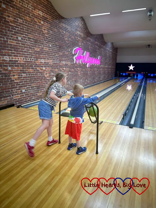 Sophie helping Thomas roll a bowling ball down a ramp towards the pins at ten-pin bowling